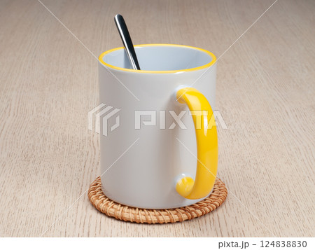 Two-tone 11oz mug on the mug coaster on the table. Mug with tea spoon. Mug with yellow handle and inner part. 124838830