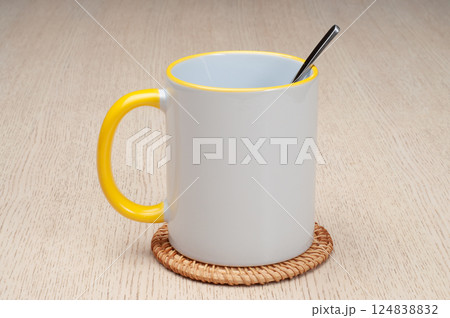 Two-tone 11oz mug on the mug coaster on the table. Mug with tea spoon. Mug with yellow handle and inner part. 124838832