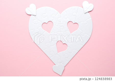 White heart-shaped jigsaw puzzle on a grey background, with several pieces missing and placed nearby. Symbolizing love, connection, or incompleteness, perfect for themes of relationships and emotions. White heart-shaped jigsaw puzzle on a grey background, with several pieces missing and placed nearby. Symbolizing love, connection, or incompleteness, perfect for themes of relationships and emotions. 124838983