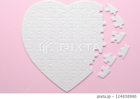 White heart-shaped jigsaw puzzle on a grey background, with several pieces missing and placed nearby. Symbolizing love, connection, or incompleteness, perfect for themes of relationships and emotions. White heart-shaped jigsaw puzzle on a grey background, with several pieces missing and placed nearby. Symbolizing love, connection, or incompleteness, perfect for themes of relationships and emotions. 124838990