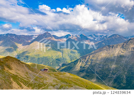 The stunning Otztal Alps showcase lush green valleys and majestic peaks under a bright blue sky with fluffy clouds. Nature thrives in this serene summer landscape, perfect for outdoor exploration. 124839634