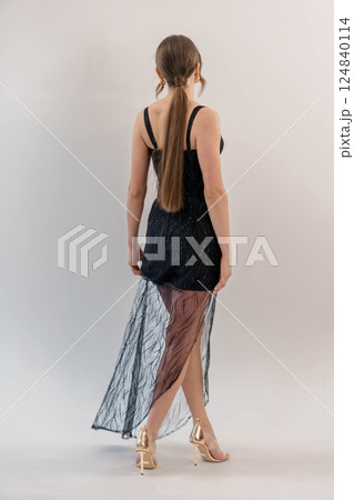 Elegant Young Woman in Stylish Black Sheer Evening Dress and Golden High Heels Posing Gracefully with Back View Elegant Young Woman in Stylish Black Sheer Evening Dress and Golden High Heels Posing Gracefully with Back View 124840114