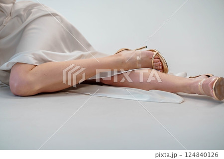 Elegantly Crossed Female Legs in Satin Dress and Stylish High Heels on Grey Background 124840126