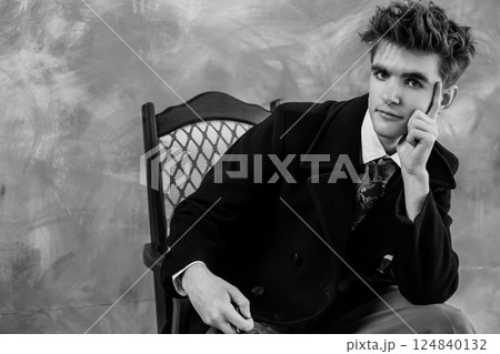 Black and white portrait of a young man in formal attire, leaning on an antique chair with a contemplative expression 124840132