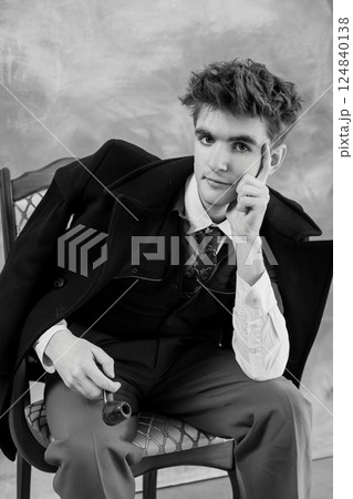 Black and white portrait of a young man in formal attire, seated with a thoughtful expression and holding a pipe 124840138