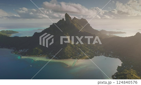 Sunset over Bora Bora's turquoise lagoon and iconic mount otemanu towering over south pacific ocean water. Dramatic beauty of French Polynesia. Remote wild nature scene, travel background. Aerial view Sunset over Bora Bora's turquoise lagoon and iconic mount otemanu towering over south pacific ocean water. Dramatic beauty of French Polynesia. Remote wild nature scene, travel background. Aerial view 124840576
