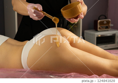 Honey flows from dipper onto lower back during body spa treatment. 124841020