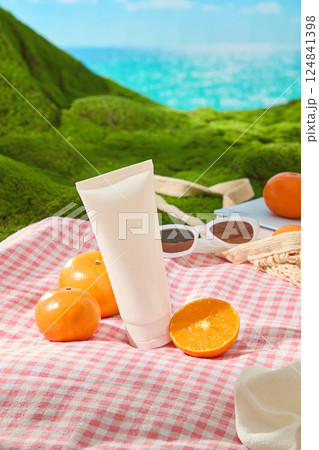 Cosmetic tube with oranges of various sizes placed on checkered carpet . Oranges reveal juicy segments. Sunglasses are placed along with a mesh bag containing notebooks displayed on green grass.  124841398