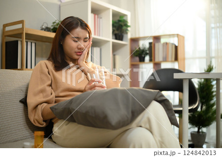 Female holding a glass of water and touching her cheek experiencing tooth sensitivity 124842013