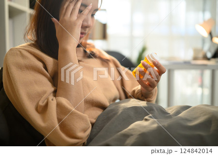 Young woman holding a bottle of medicine while suffering from illness Young woman holding a bottle of medicine while suffering from illness 124842014