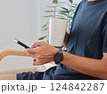 Man's hand holding coffee cup and using smartphone Sitting at sofa in Living room. 124842287
