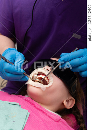 Young child receiving dental treatment with a calm expression in a modern clinic, surrounded by professional equipment during a bright afternoon appointment 124842409