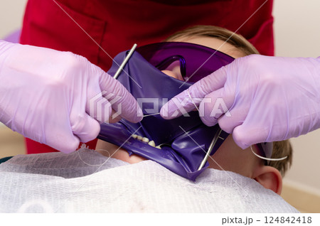 Young child experiencing dental care with protective eyewear in modern clinic as dentist uses specialized tools for treatment on a bright afternoon 124842418