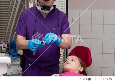 Young girl receiving dental care in a modern clinic with a professional smiling dentist wearing gloves and goggles, ensuring comfort during the procedure 124842419