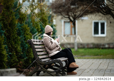 Person enjoying a quiet moment on a park bench while engaging with a mobile device amidst lush greenery and cozy surroundings Person enjoying a quiet moment on a park bench while engaging with a mobile device amidst lush greenery and cozy surroundings 124842614