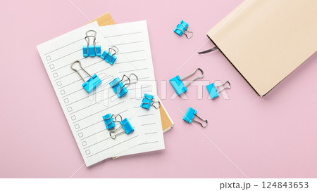 Blue binder clips on checklist paper with notebook on pink background Blue binder clips on checklist paper with notebook on pink background 124843653