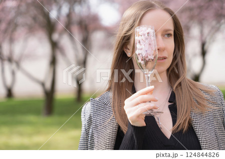 Young woman holding champagne glass with cherry blossoms in front of her eye in Prague spring park Young woman holding champagne glass with cherry blossoms in front of her eye in Prague spring park 124844826