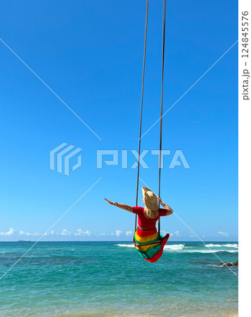 female traveller in a dress and wide-brimmed hat on a swing 124845576