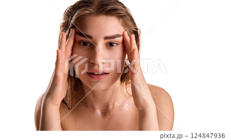 Portrait of young pretty girl with sparkles on skin, looking at camera and framing her face against white background. 124847936