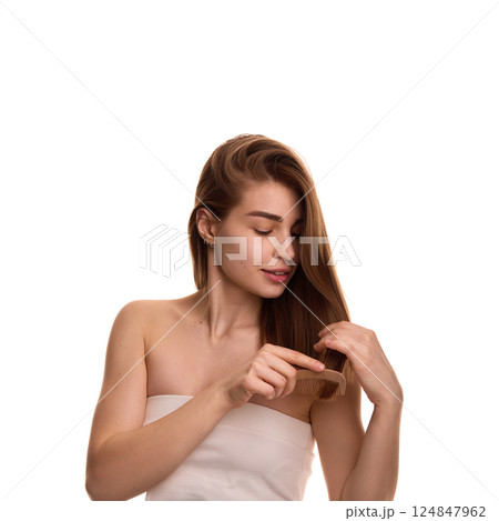 Photo of young pretty woman, combing her, long, well groomed shiny hair against white background. Hairstyling. 124847962