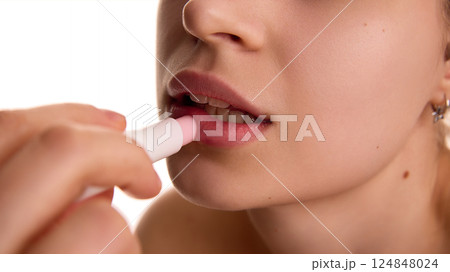Extremely close up of female model applying, moisturizing, proactive lip balm on lips against white background. 124848024