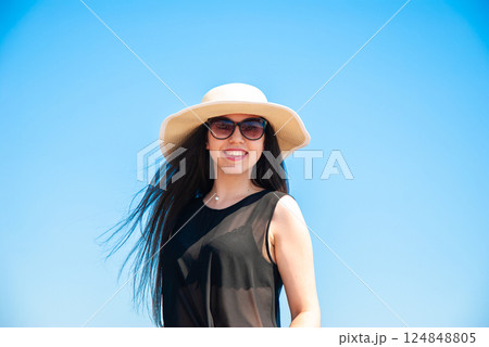 Smiling woman in sun hat and sunglasses enjoying a sunny day outdoors. Happy summer days, travel and vacation concept 124848805