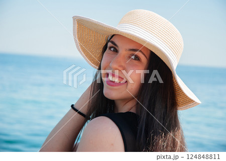 Joyful woman with sun hat smiling by the ocean on a sunny day. Happy summer days, travel and vacation concept 124848811