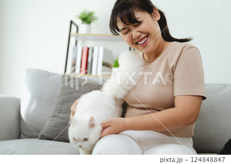An Asian woman is playing with a white Persian cat in the living room. 124848847