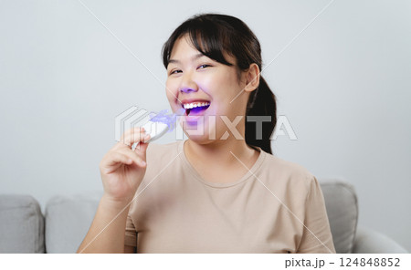 The woman is whitening her teeth with a teeth whitening device by herself The woman is whitening her teeth with a teeth whitening device by herself 124848852
