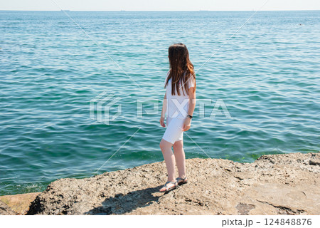 Woman enjoying a sunny day by the ocean on a rocky shoreline. Happy summer days, travel and vacation concept 124848876