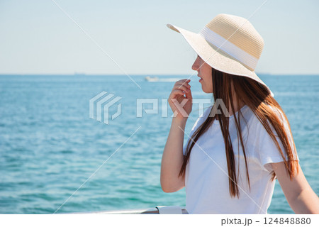 Young woman in sun hat enjoying a scenic summer day by the sea. Happy summer days, travel and vacation concept 124848880