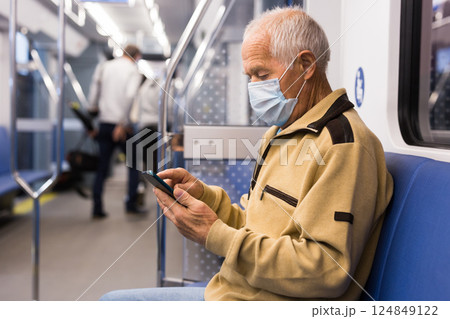 Mature passenger in protective mask using mobile phone in subway to entertain during transportation Mature passenger in protective mask using mobile phone in subway to entertain during transportation 124849122
