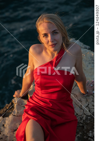 woman in red dress sitting on a rock by the sea woman in red dress sitting on a rock by the sea 124849807
