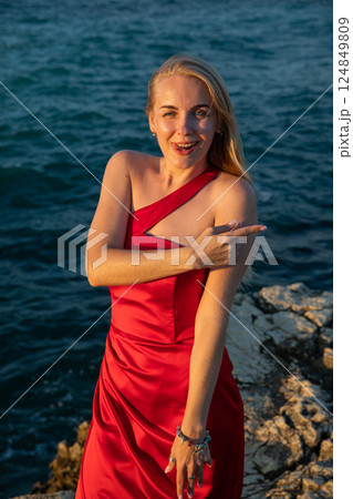 woman in red dress sitting on a rock by the sea woman in red dress sitting on a rock by the sea 124849809