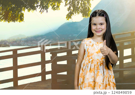 Portrait of a little caucasian girl showing like gesture outdoors. Sea resort vacation background with a wooden bridge. Portrait of a little caucasian girl showing like gesture outdoors. Sea resort vacation background with a wooden bridge. 124849859