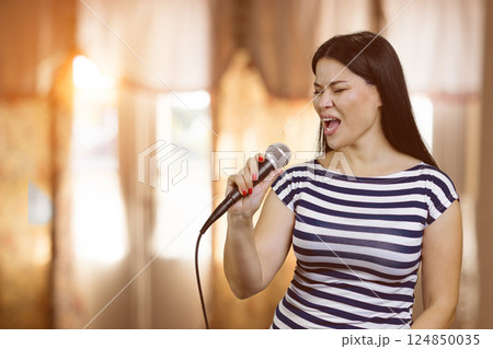 Portrait of singing asian woman with microphone. Blurred windows indoor background. Portrait of singing asian woman with microphone. Blurred windows indoor background. 124850035