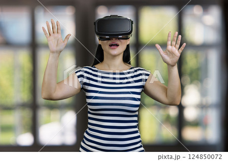 Amazed woman in vr headset with her hands up. Blurred checkered windows background. Amazed woman in vr headset with her hands up. Blurred checkered windows background. 124850072