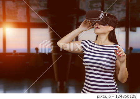 Young woman wearing virtual reality in headset. Dark room with evening sunlight on the background. Young woman wearing virtual reality in headset. Dark room with evening sunlight on the background. 124850129