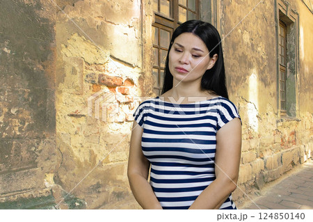Young pensive sad woman of Asian ethnicity. Shabby building background. 124850140