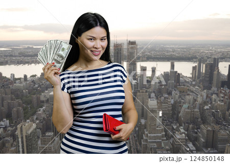 Young asian woman is holding fan of dollars from a red wallet. Urban cityscape background. Young asian woman is holding fan of dollars from a red wallet. Urban cityscape background. 124850148