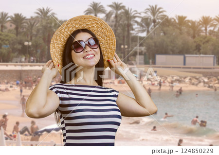Happy young woman with straw hat standing outdoors. Beach resort background. Happy young woman with straw hat standing outdoors. Beach resort background. 124850229