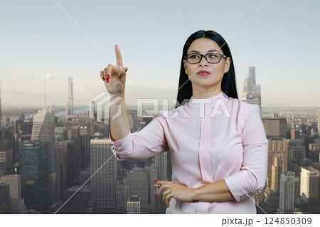 Young asian woman touching invisible virtual screen with her finger. Urban cityscape background. 124850309