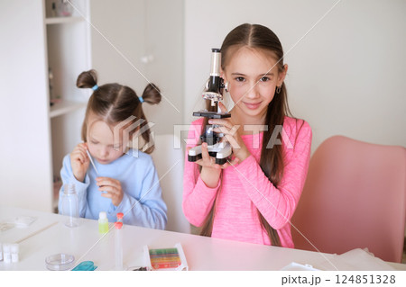 A girl demonstrates a microscope for children's experiments at home. Pre-school education 124851328