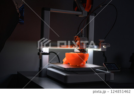 3D Printer Creating Orange Plastic Object on Platform 124851462