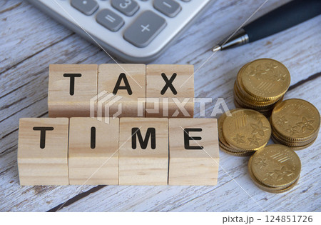Top view of Tax Time text on wooden cubes surrounded by gold coins and calculator 124851726
