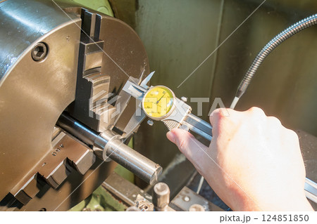 The machine operator measure the thickness of the metal shaft parts with dial vernier caliper. The machine operator measure the thickness of the metal shaft parts with dial vernier caliper. 124851850