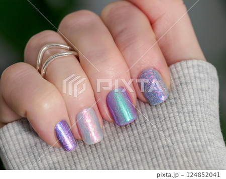 Skittles nails on hand. Colorful shiny manicure with different textures in light purple tones, pink and lilac hue. Closu-up of female hand with multicolored nails on green foliage background. Copy Skittles nails on hand. Colorful shiny manicure with different textures in light purple tones, pink and lilac hue. Closu-up of female hand with multicolored nails on green foliage background. Copy 124852041