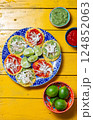 Vibrant chalupas with green and red sauces served on a decorative plate beside limes and bowls of salsa 124852063