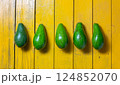 Fresh green avocados lined up on a vibrant yellow wooden surface during daylight 124852070