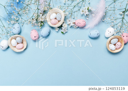 Flat lay of Easter eggs, decorative nests, and blue feathers on pastel blue background, greeting card concept with festive spring design Flat lay of Easter eggs, decorative nests, and blue feathers on pastel blue background, greeting card concept with festive spring design 124853119